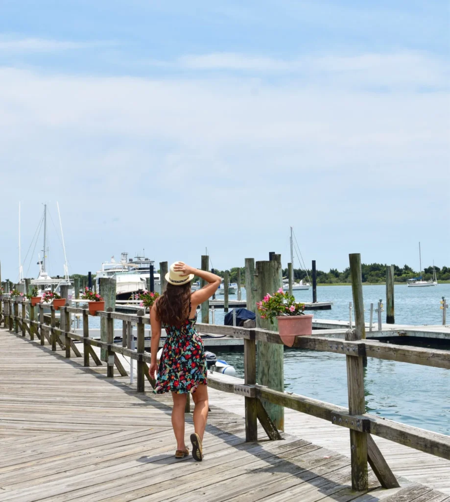 kate storm in a floral dress on the boardwalk in beaufort north carolina facing away from camera and toward water and parked boats